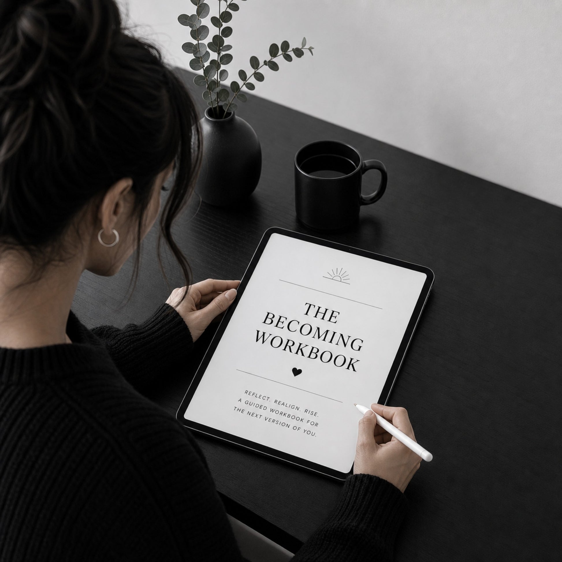 The Becoming Workbook self-reinvention guide on a tablet — black desk scene with coffee and eucalyptus